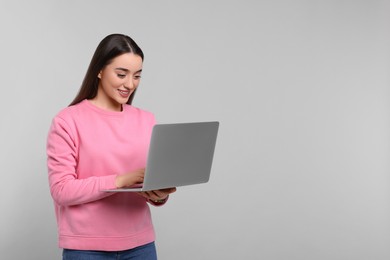 Smiling young woman working with laptop on grey background, space for text