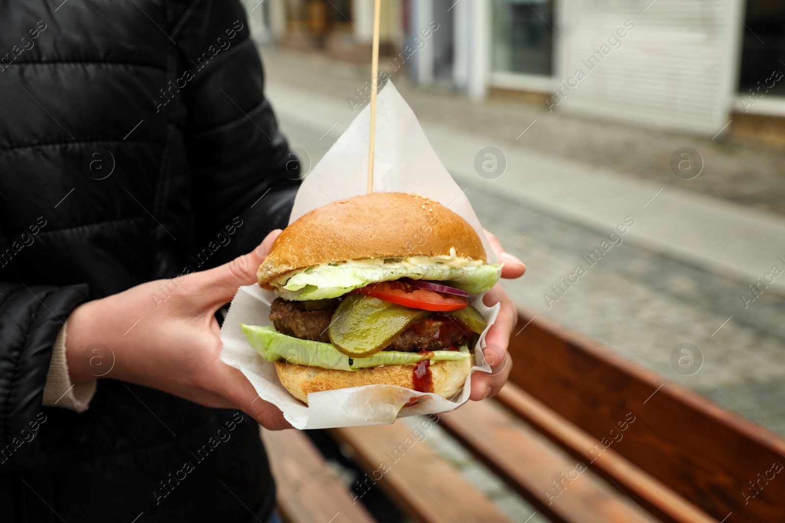 Photo of Woman holding fresh delicious burger outdoors, closeup. Street food