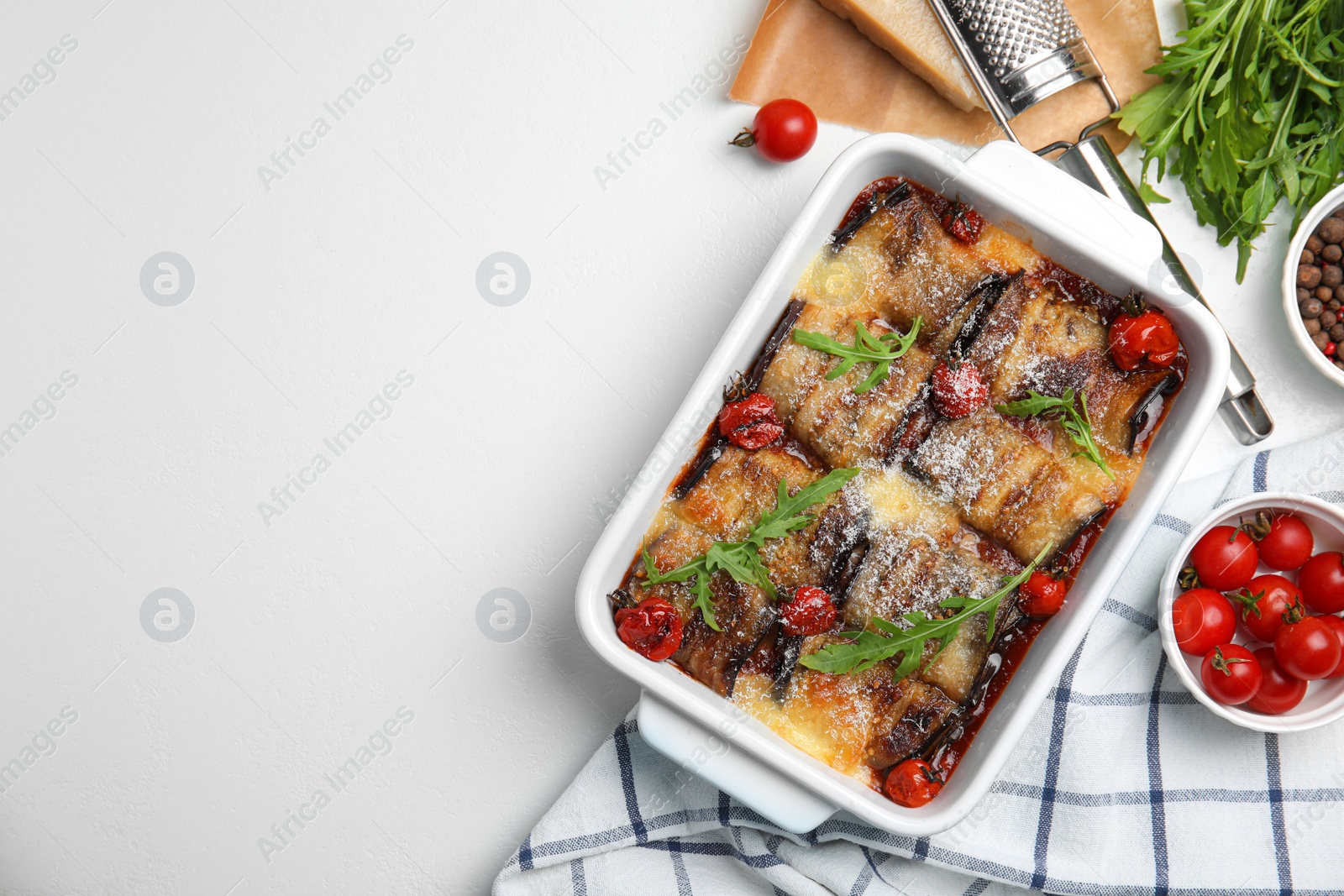 Photo of Tasty eggplant rolls with tomatoes, cheese and arugula in baking dish on white table, flat lay. Space for text