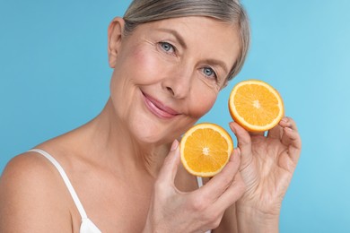 Photo of Beautiful woman with halves of orange rich in vitamin C on light blue background