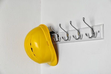 Photo of Hard hat hanging on white wall. Safety equipment