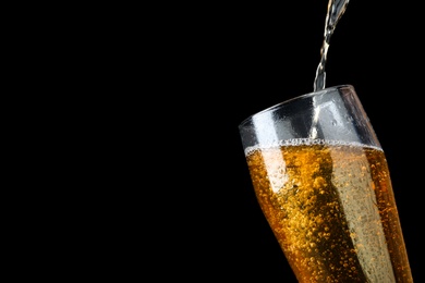 Photo of Pouring cold tasty beer into glass on black background, closeup. Space for text