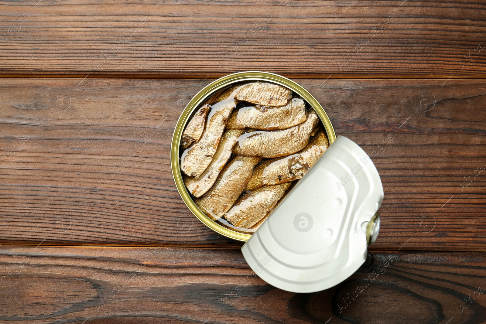 Photo of Open tin can of sprats on wooden table, top view