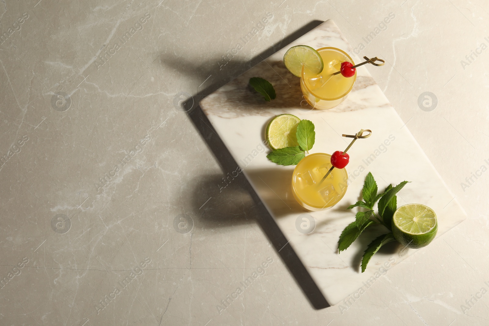 Photo of Glasses of tasty pineapple cocktail decorated with cherry and lime on light grey marble table, top view. Space for text