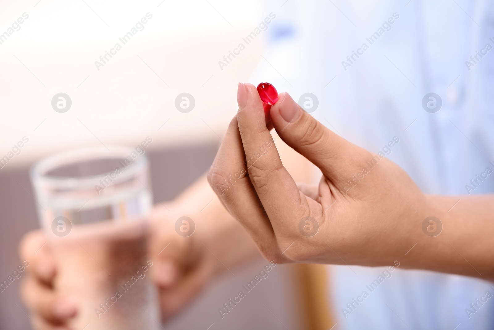 Photo of Woman holding pill and glass of water on blurred background, closeup. Space for text