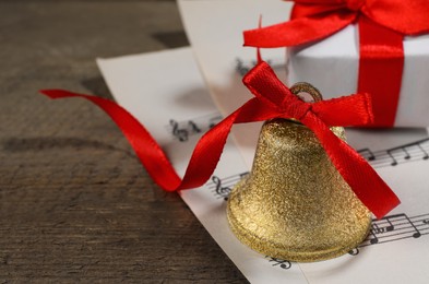 Photo of Bell, gift box and music sheets on wooden table, closeup with space for text. Christmas decor