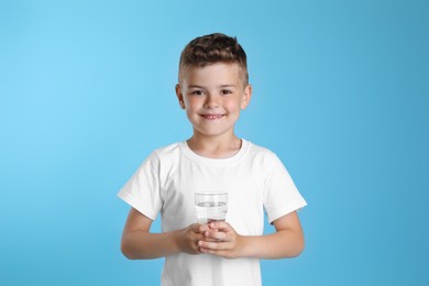 Photo of Cute little boy with glass of water on light blue background