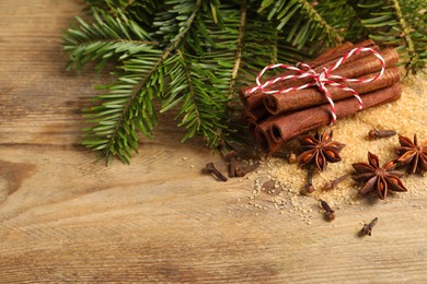 Different spices and fir branches on wooden table, flat lay. Space for text