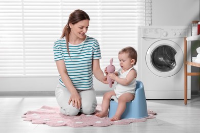Photo of Mother training her child to sit on baby potty indoors