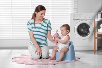 Mother training her child to sit on baby potty indoors