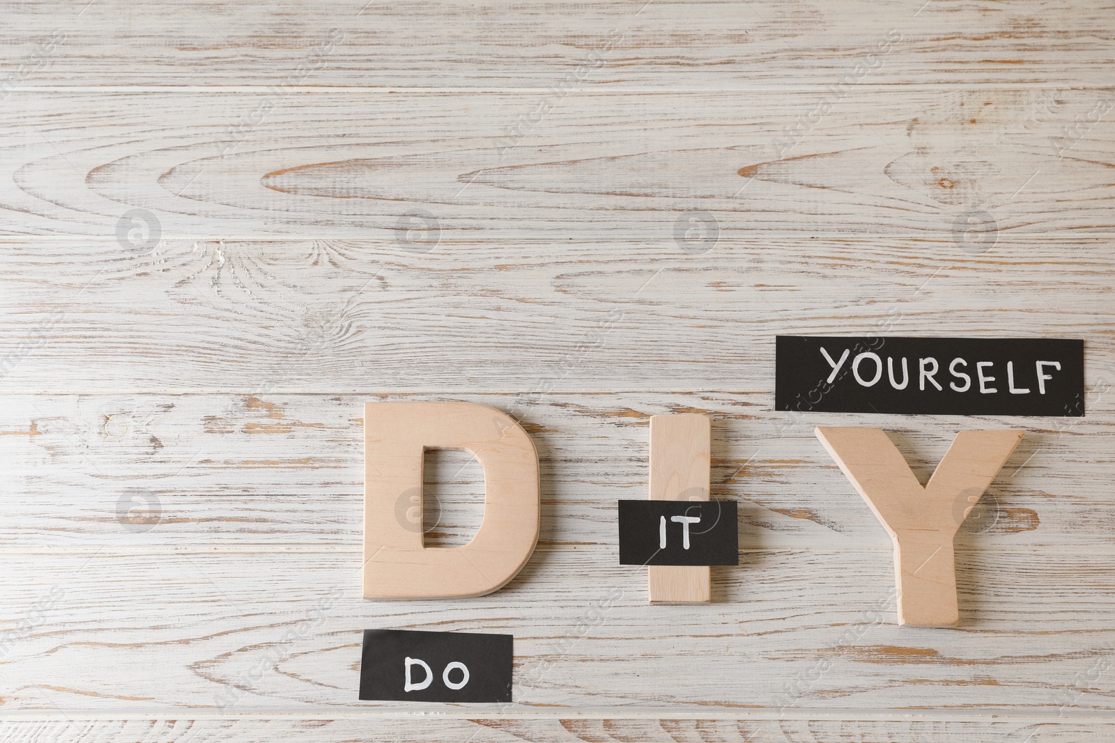 Photo of Phrase Do It Yourself and abbreviation DIY made of letters on white wooden table, flat lay. Space for text