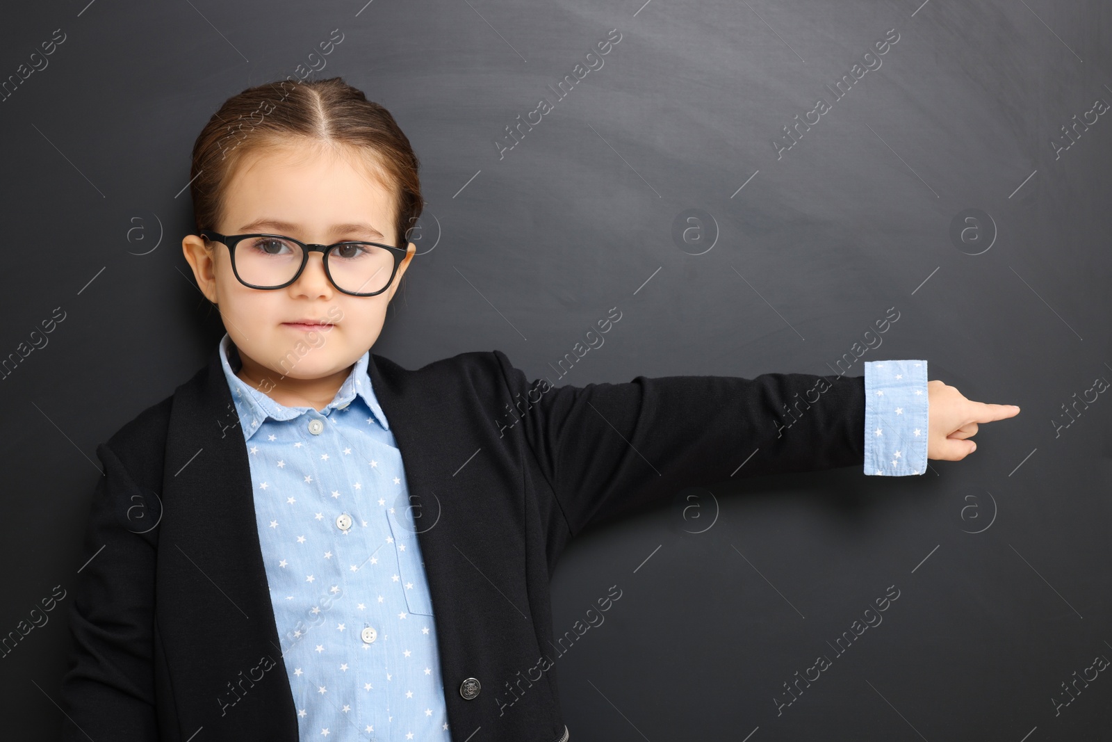 Photo of Little school child in uniform pointing at something near chalkboard