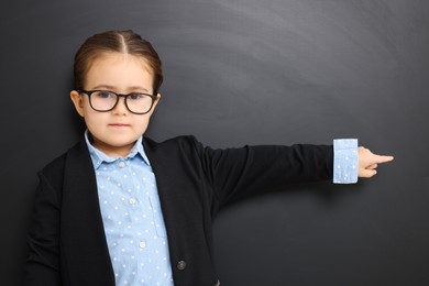 Little school child in uniform pointing at something near chalkboard