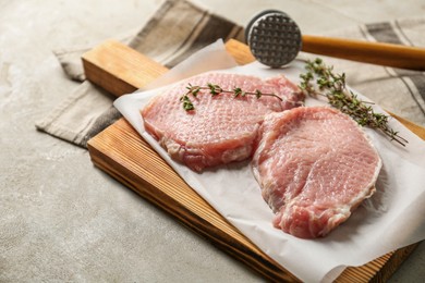 Photo of Cooking schnitzel. Raw pork chops, thyme and meat mallet on grey table