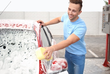 Young man cleaning vehicle with sponge at self-service car wash