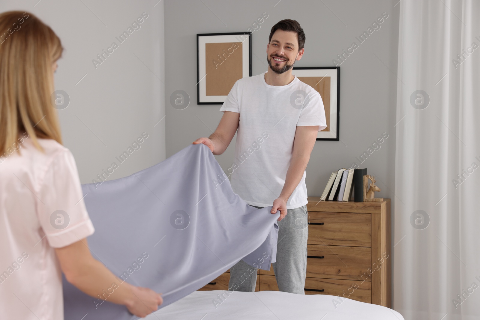 Photo of Couple changing bed linens in room. Domestic chores