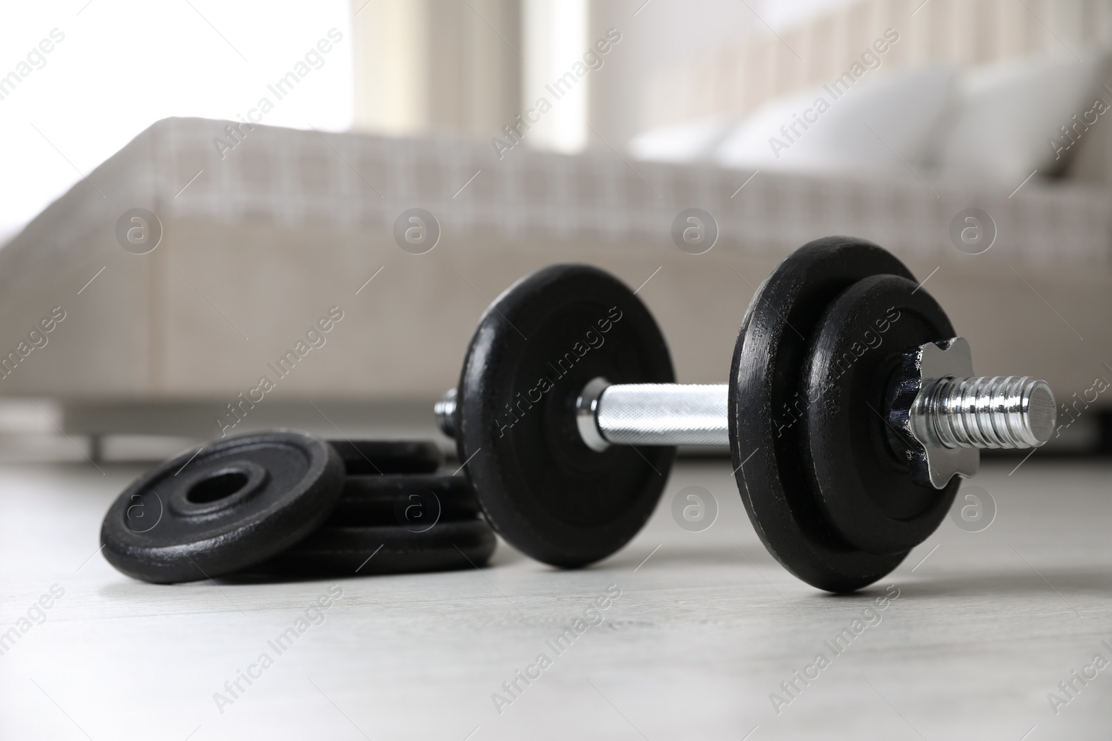 Photo of Steel dumbbell and weight plates on floor indoors. Fitness at home