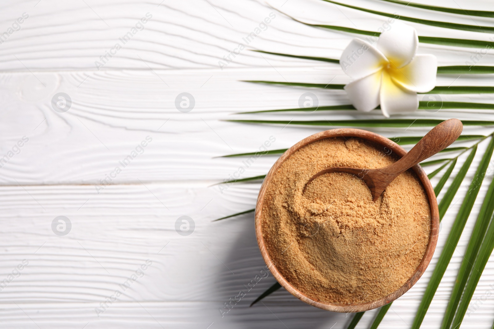 Photo of Coconut sugar and spoon in bowl on white wooden table, flat lay. Space for text