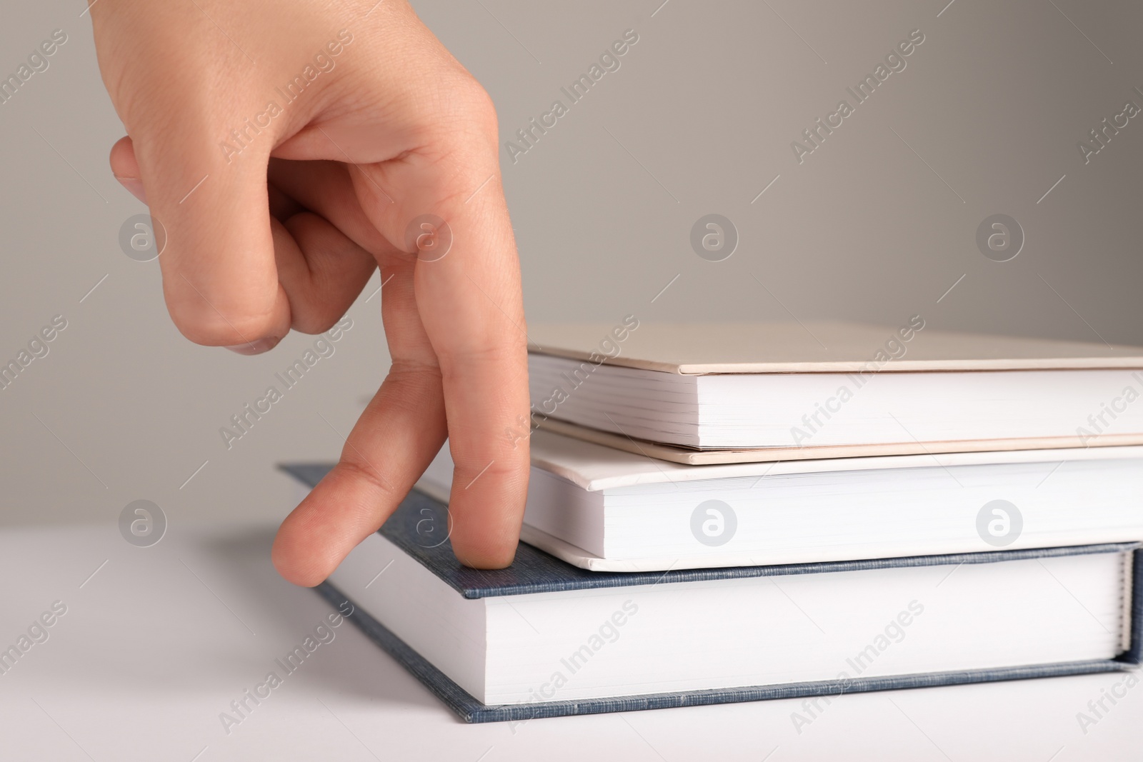 Photo of Woman imitating stepping up on books with her fingers against grey background, closeup