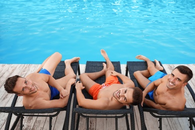 Happy young friends relaxing on deck chairs near swimming pool