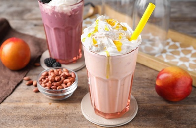 Photo of Tasty peach and blackberry milk shakes in glasses on wooden table