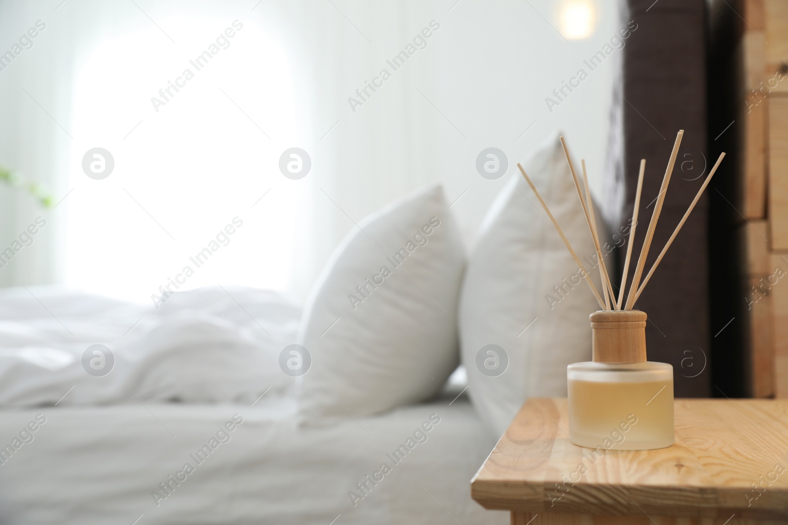 Photo of Reed diffuser on nightstand near bed in room. Modern interior