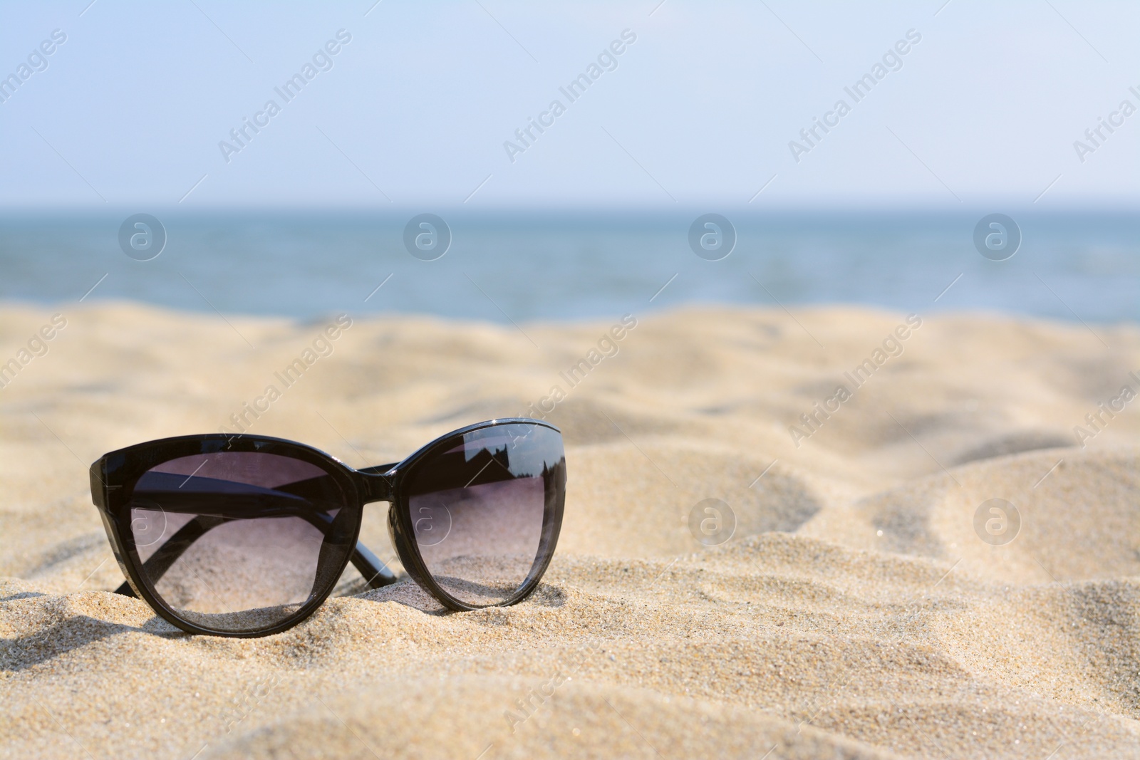 Photo of Stylish sunglasses on sandy beach near sea, space for text