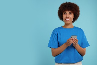 Photo of Happy young woman with smartphone on light blue background. Space for text