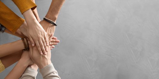 Photo of People holding hands together over grey stone background, top view with space for text. Unity concept