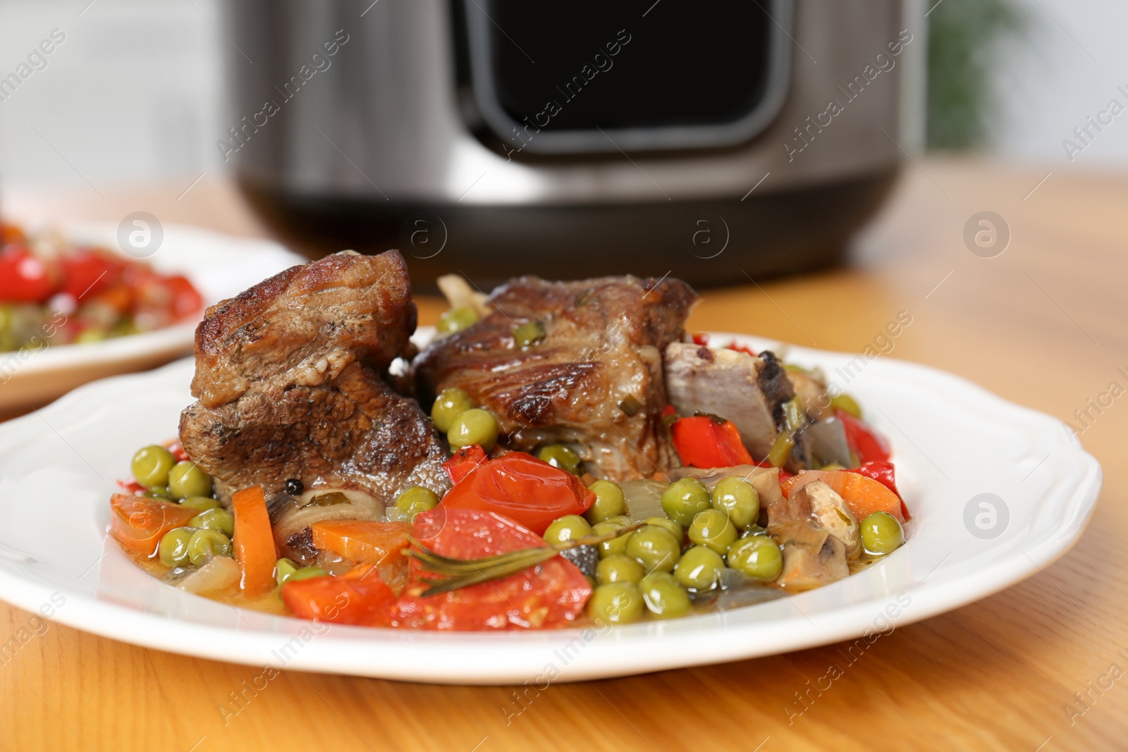 Photo of Plate with meat and garnish prepared in multi cooker on table, closeup