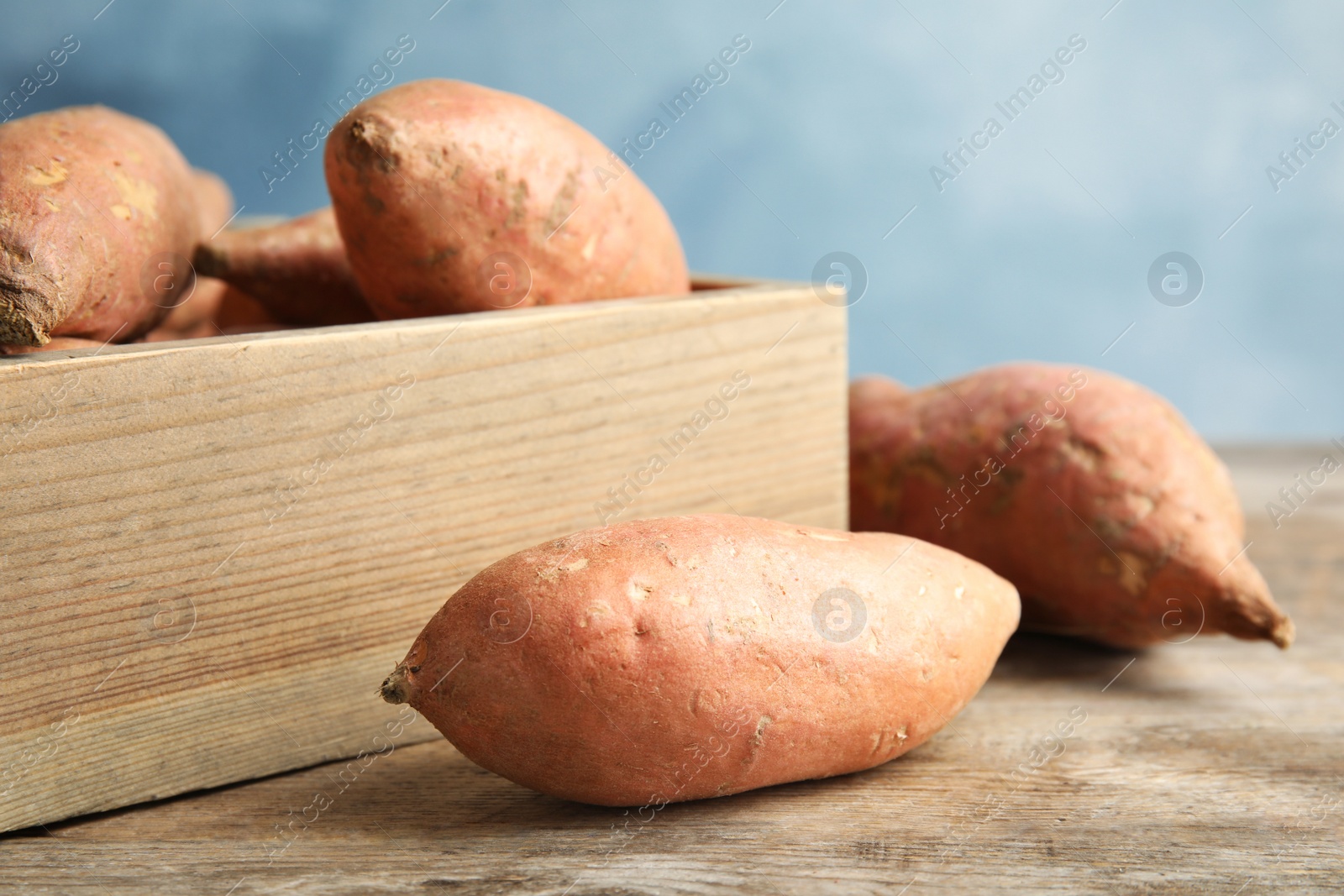 Photo of Sweet potatoes and wooden crate on table against color background