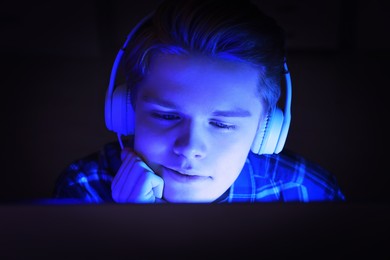 Internet addiction. Teenage boy in headphones using device at night. Toned in blue