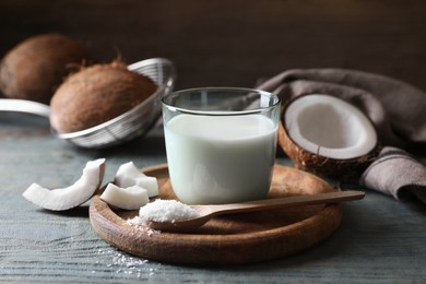Photo of Glass of delicious coconut milk, spoon with flakes and nuts on wooden table