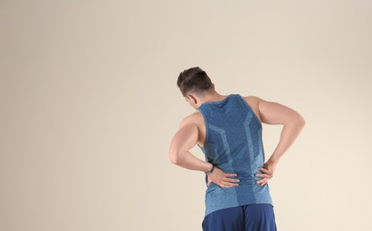 Photo of Man in sportswear suffering from back pain on light background