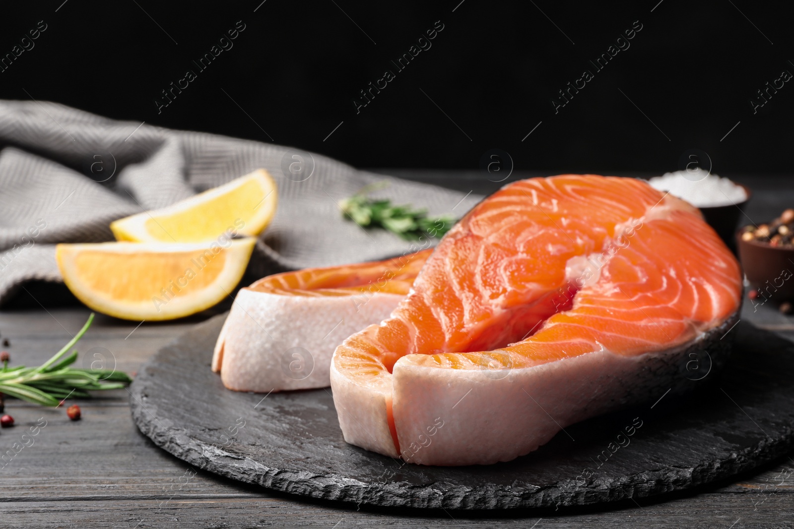Photo of Fresh salmon steaks on black wooden table, space for text