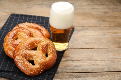 Photo of Tasty pretzels and glass of beer on wooden table, space for text