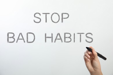 Image of Woman writing phrase Stop Bad Habits on glass against white background, closeup