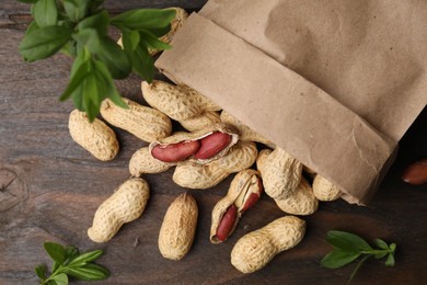 Photo of Paper bag with fresh peanuts and leaves on wooden table, flat lay