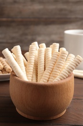 Photo of Bowl with wafer rolls on wooden table, closeup