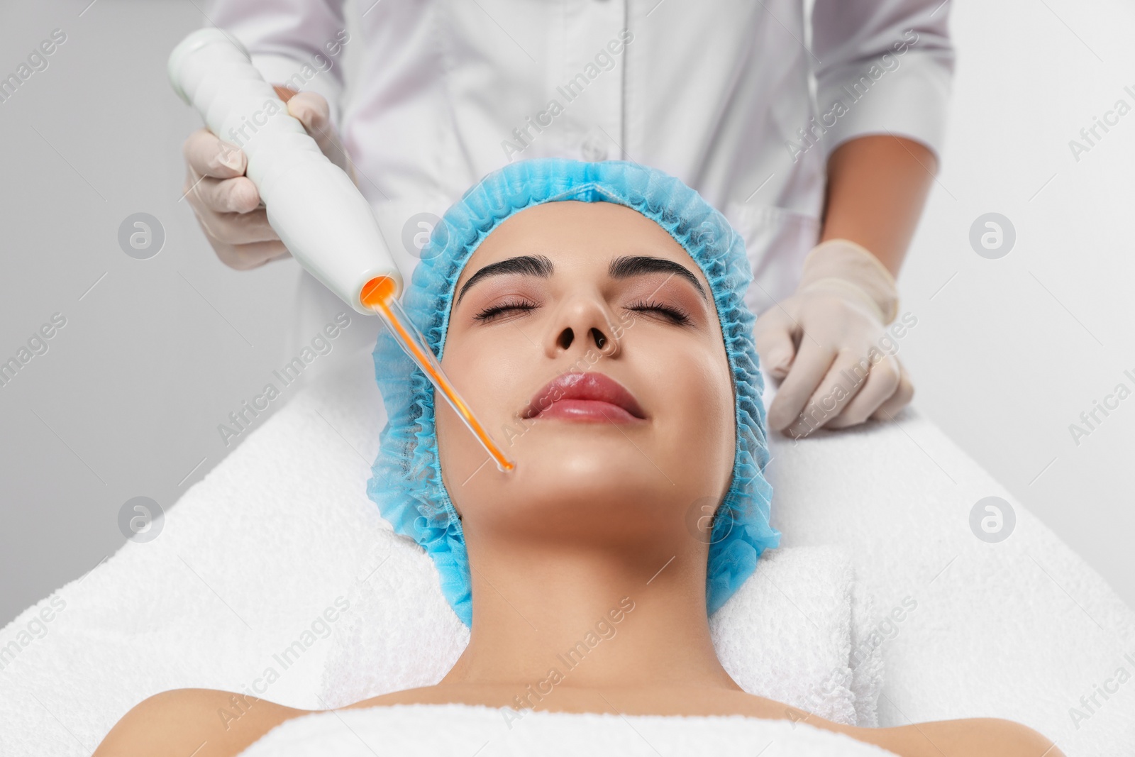 Photo of Young woman undergoing face rejuvenation procedure with darsonval in salon