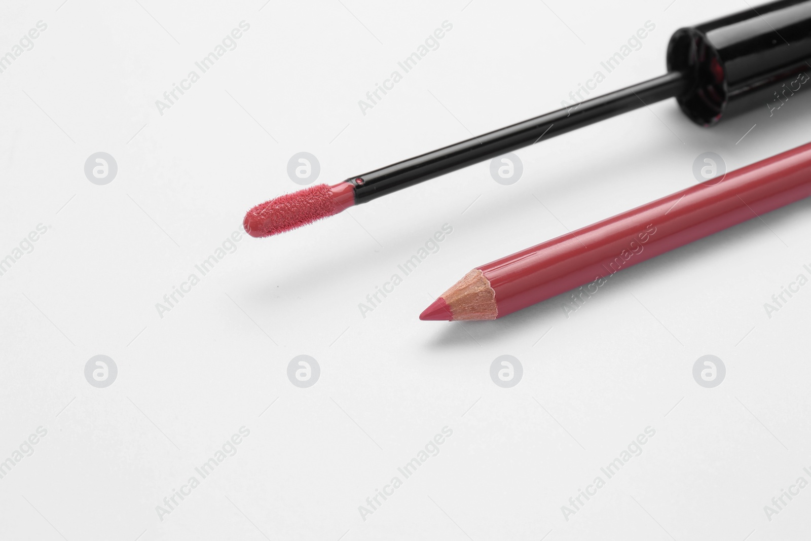 Photo of Lip pencil and brush of liquid lipstick on white background, closeup. Cosmetic product