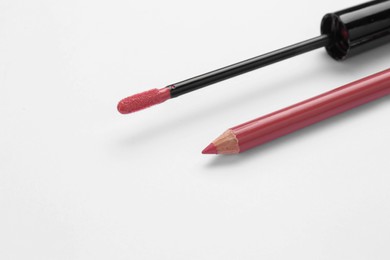 Lip pencil and brush of liquid lipstick on white background, closeup. Cosmetic product