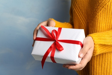 Photo of Young woman holding Christmas gift on blue background, closeup