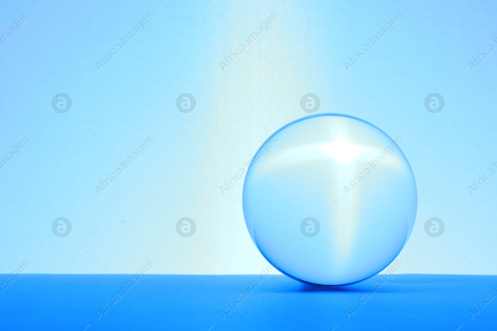 Photo of Transparent glass ball on table against light blue background. Space for text