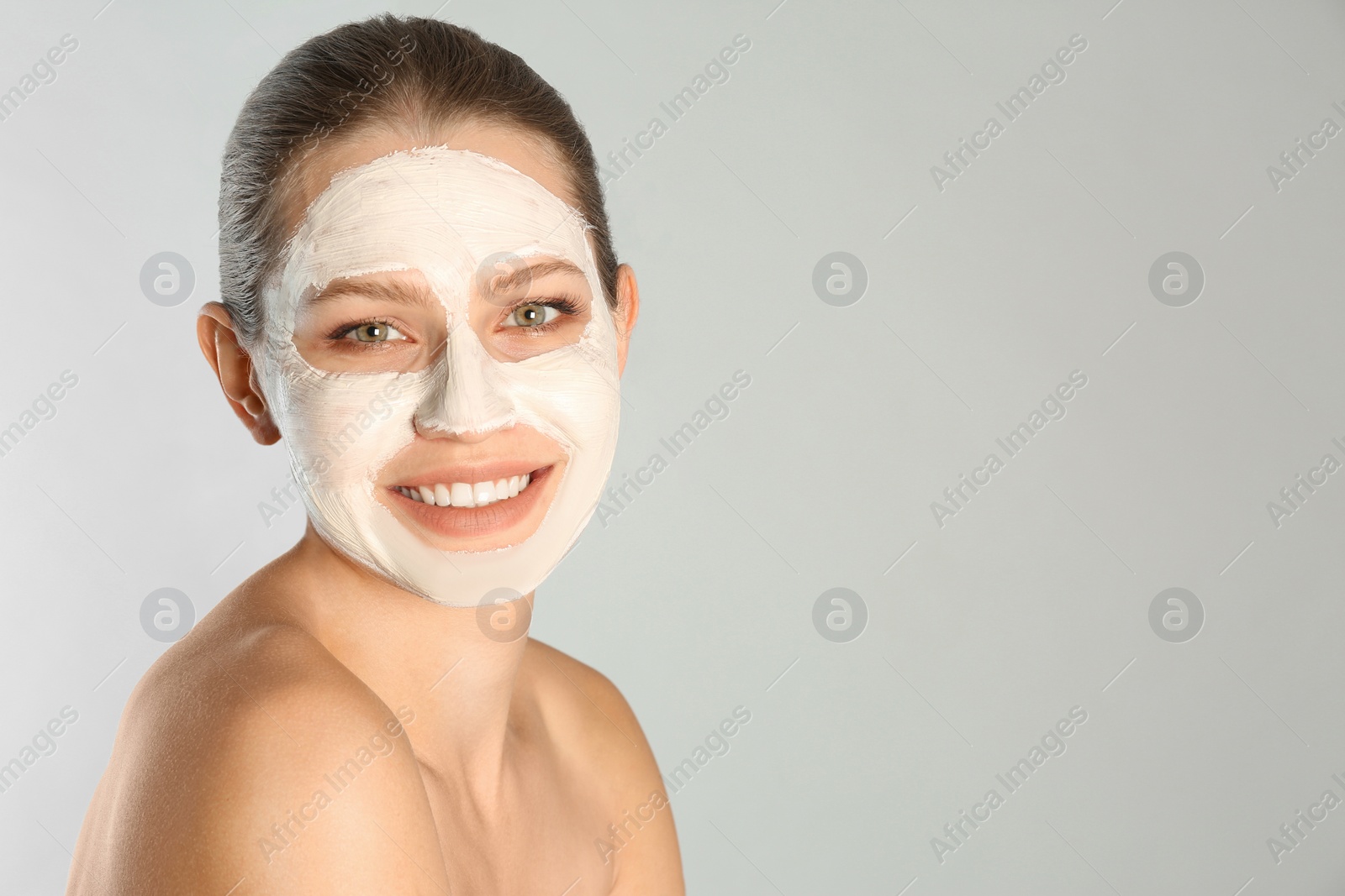 Photo of Beautiful woman with clay mask on her face against grey background. Space for text