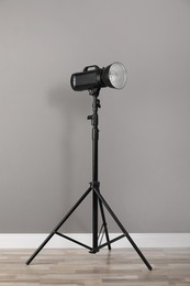 Photo of Professional studio flash light with reflector on tripod near grey wall in room. Photography equipment
