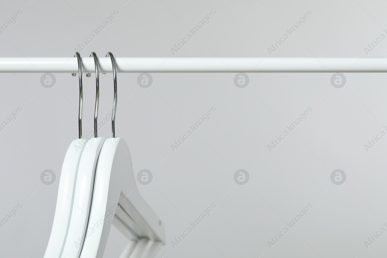 Photo of Empty clothes hangers on rack against light grey background, closeup. Space for text