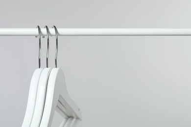 Photo of Empty clothes hangers on rack against light grey background, closeup. Space for text