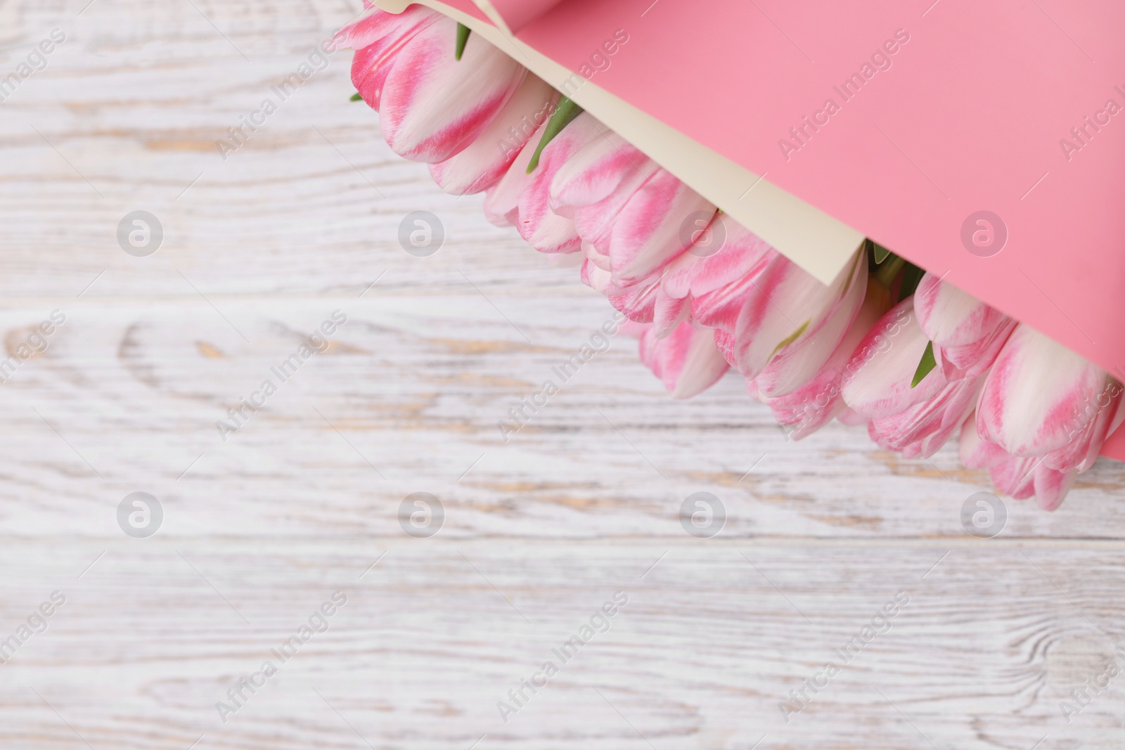 Photo of Beautiful bouquet of fresh pink tulips on white wooden table, top view. Space for text