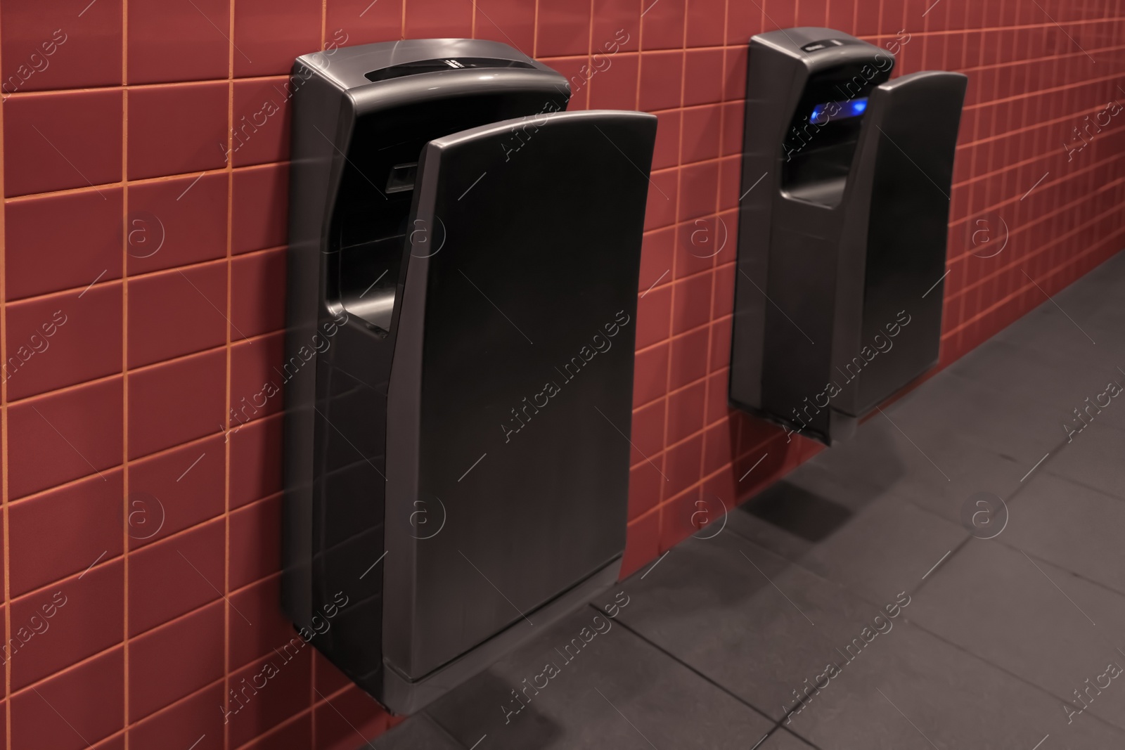 Photo of Modern hand dryers on tiled wall in public toilet